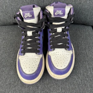Nike Air Jordans i lila och svart - Snygga Nike Air Jordans med en cool kombination av lila och svart. Skorna har en klassisk hög design med Zoom Air-detaljer och svart snörning. Perfekta för att ge din stil ett lyft.