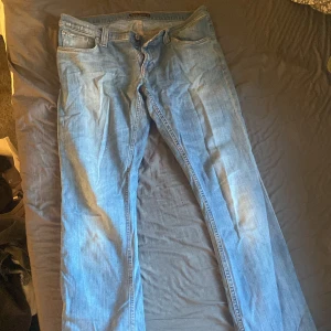Blå jeans från Nudie Jeans - Säljer ett par klassiska blå jeans från Nudie Jeans. De har en normal passform och är tillverkade i en bomullsblandning med lite stretch för extra komfort. Perfekta för en avslappnad stil.