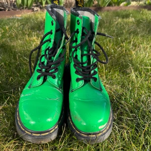 Gröna boots från Dr. Martens - Säljer ett par gröna boots från Dr. Martens med klassisk snörning och robust sula. Perfekta för att ge din stil en färgklick. De har en ikonisk design med gula sömmar och svart snörning. I storlek 37. 