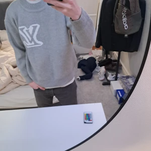 Grå tröja från Louis Vuitton - Säljer en stilren grå tröja från Louis Vuitton med ett stort vitt LV-märke på framsidan och på baksidan. Tröjan har långa ärmar och ribbade muddar vid ärmslut och nederkant. Perfekt för en trendig look.