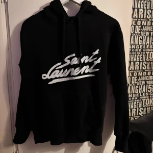 Svart hoodie från Saint Laurent - Säljer en snygg svart hoodie från Saint Laurent med deras logga på framsidan. Säljer då den är för liten för mig. Bra skick förutom ett litet hål på längst nere på armen. Skriv för frågor!