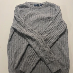 Grå stickad tröja från Gant - Säljer en stilren grå stickad tröja från Gant med kabelstickat mönster. Och är i ett superbra skick 9/10