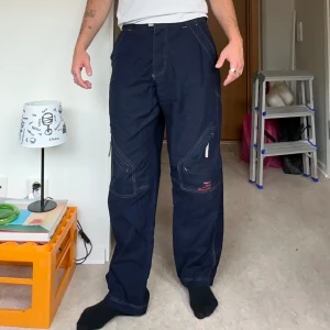 Mörkblå cargopants från H2O Sportswear - Säljer ett par mörkblå cargopants från H2O Sportswear sitter som W32 L32. Byxorna har flera praktiska fickor, kontrastsömmar och en loose passform. Perfekta för dig som gillar streetwear och funktionella detaljer.