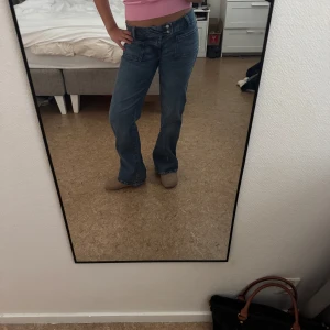 Lågmidjade blå baggy bootcut jeans - Säljer ett par blå jeans med låg midja och bootcut-modell. Jeansen har två stora fickor framtill och dubbla knappar i midjan. Perfekt passform, har sytt in de från insidan i midjan vilket inte syns utåt, går lätt att klippa bort, använt några få gånger, storlek M short
