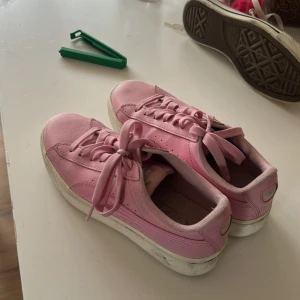 Rosa sneakers från Puma, strl 37 - Snygga rosa sneakers från Puma i storlek 37. Skorna har klassisk låg modell med rund tå, snörning och vit platt sula. Tillverkade i syntetmaterial med diskret Puma-logga på sidan. Perfekta för dig som vill ha en poppig färg på fötterna.