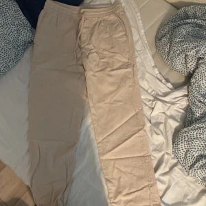 Beiga linnebyxor med resårmidja - Snygga och luftiga beiga linnebyxor med resår i midjan och sidfickor. Perfekta för varma dagar och ger en avslappnad vibe. Raka ben och enkel design som passar till det mesta. Sköna att bära och lätta att matcha med olika toppar.