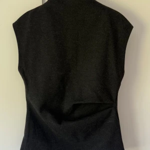 Grå topp med minimalistisk look - En stilren svart topp i ull med enkel, rak passform och ärmlös design. Toppen har en minimalistisk look utan synliga detaljer eller mönster, perfekt för att bygga lager eller skapa en clean outfit.