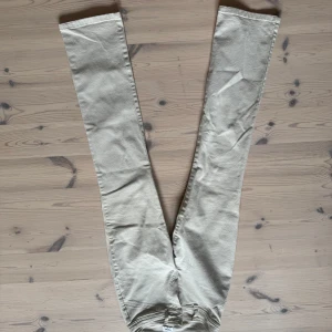 Beiga raka jeans från Flippak - Snygga beiga jeans från Flippak i rak modell. Byxorna har hög midja, klassiska fickor och stängs med två metallknappar och dragkedja. Perfekta till en avslappnad och stilren look. Matrialet är stretchigt