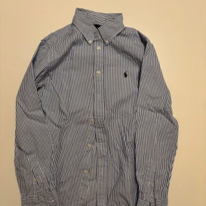 Randig skjorta från Ralph Lauren - Klassisk skjorta från Ralph Lauren i blåvitt randigt mönster. Riktigt bra skick med inga defekter i storlek y14