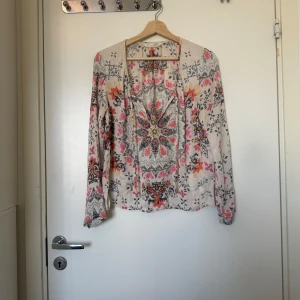 Blommig blus med färgglatt mönster - Supersöt blus med blommigt och bohemiskt mönster i rosa, gul, blå och svart på en ljusbeige bas. Långärmad och luftig modell med v-ringning och snygga detaljer framtill. Perfekt för dig som gillar färg och mönster! Från märket Odd Molly i storlek 1 som ungefär motsvarar en storlek S. Mycket fint skick, jag hittar inga synlig anmärkningar eller defekter.  