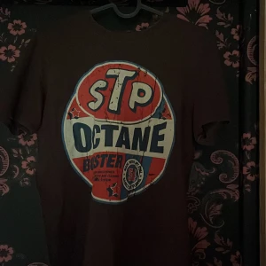 Brun STP Octane t-shirt med tryck - Cool brun t-shirt med stort vintageinspirerat STP Octane-tryck i rött, vitt och blått på bröstet. Klassisk passform och rund hals. Perfekt för dig som gillar retrostil och statement-plagg.