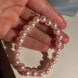Rosa pärlarmband  - Sött armband med ljusrosa pärlor på  rosa tråd. Pärlorna är runda och har en glansig finish som ger ett stilrent och gulligt intryck. Perfekt accessoar för att addera lite färg och shimmer till din look.
