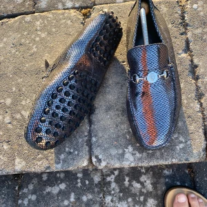 Gucci loafers i svart ormskinn - Snygga loafers från Gucci i svart ormskinnsmönster med metallspänne framtill. Skorna har rund tå och platt sula med gummidetaljer undertill för extra grepp. Lyxig känsla och perfekt för dig som vill sticka ut med exklusiva detaljer.