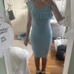 Ljusblå ribbad kortklänning med volang - Supersöt ljusblå kortklänning med ribbat tyg och volangdetalj över axlarna. Klänningen är ärmlös och har en figurnära passform som framhäver siluetten. Perfekt för dig som gillar en feminin och trendig look!