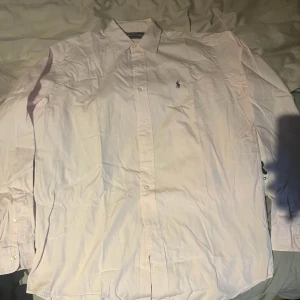Ralph Lauren skjorta - Säljer en klassisk ljusrosa skjorta från Polo Ralph Lauren med broderad logga på bröstet. Perfekt för dig som gillar stilrena och tidlösa plagg. Skjortan är i storlek 38/M men passar även L. Skriv för mer frågor!