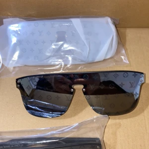 Svarta Louis Vuitton solglasögon shield - Snygga svarta shield-solglasögon från Louis Vuitton med LV-monogram på glaset. Raka, breda bågar i svart och speglande linser ger en futuristisk vibe. Perfekta för dig som vill sticka ut och köra på en lyxig streetstyle-look. Helt Nya par.