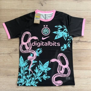 Inter Milan x Nike svart fotbollströja S - Unik Inter Milan fotbollströja från Nike i svart med rosa och turkosa detaljer. Tröjan har korta ärmar, rosa ormmotiv och växtgrafik, samt rosa muddar och krage. Digitalbits-logga på bröstet och klubbmärke i turkos. Tillverkad i lätt och ventilerande material.