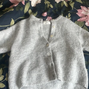 Grå stickad kofta från Gina Tricot -  ribbstickad grå kofta från Gina Tricot i ullblandning. Kortärmad modell med snygga vita knappar framtill. Perfekt att slänga över ett linne eller t-shirt är en kofta som sticks. Säljer koftan för att den egentligen är i storlek S men har krympt lite i tvätten så tycker inte den sitter lika fint på mig längre så skulle säga att den är något i mellan S och XS. Koftans tecken på användning är att den blivit lite luddig men inget mer vad jag har sett. Nypris är 400kr