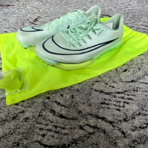Nike maxfly löparspikes - Nike maxly löparspikes. Köptes för ett år sedan och har endast använts ett fåtal gånger. Skorna har en lätt och luftig ovandel i syntetmaterial och är designade för maximal fart på banan. Säljes med tillhörande neonfärgad påse och extra dubbar.