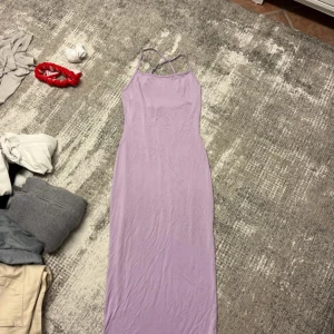 Ljuslila långklänning med smala axelband - Säljer en superfin långklänning i ljuslila med smala axelband som korsas i ryggen. Klänningen har en tight passform och ärmlös design, perfekt för dig som gillar en enkel men snygg stil. Materialet känns mjukt och följsamt mot kroppen.