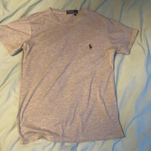 Grå t-shirt från Polo Ralph Lauren - Snygg grå t-shirt från Polo Ralph Lauren med klassisk logga på bröstet. T-shirten har rund hals, korta ärmar och är gjord i mjuk bomull. Perfekt basic-plagg med stilren look och bekväm passform.