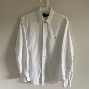 Vit skjorta Polo Ralph Lauren slim fit - Klassisk vit skjorta från Polo Ralph Lauren i slim fit-modell. Skjortan har långa ärmar, knappar framtill och den ikoniska broderade polospelaren på bröstet. Tillverkad i mjuk bomull och passar perfekt till en clean och stilren look.