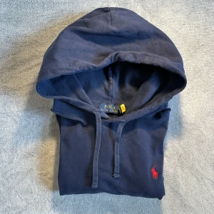 Marinblå hoodie från Polo Ralph Lauren - Snygg marinblå hoodie från Polo Ralph Lauren med klassisk röd broderad logga på bröstet. Tröjan har huva med snörning och är tillverkad i mjuk bomull. Nypris ~1600 Skick 8/10 Pris kan diskuteras vid snabbt köp.