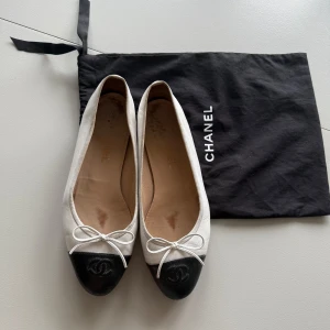 Chanel ballerinaskor i svart och vitt skinn - Klassiska ballerinaskor från Chanel i vitt skinn med svart tå. Medföljer original dustbag. Beställt från Vestiaire Collective. 