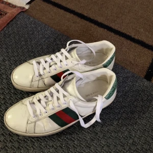 Gucci Ace vita sneakers med röd/grön rand - Gucci Ace sneakers i vitt skinn med klassiska gröna och röda ränder på sidan, helt okej skick och perfekta inför sommaren, pris är inte hugget i sten 