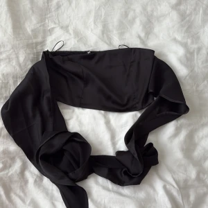 Svart bandeau tubtopp från Bik Bok - Supersnygg svart bandeau tubtopp från Bik Bok med breda knytband framtill som kan stylas till en stor rosett. Toppen har smockad baksida för extra stretch och sitter tajt. Perfekt till sommarens alla outfits!