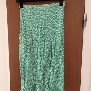 Grönvit långkjol med mönster - Snygg långkjol i grönt och vitt med ett unikt mönster. Kjolen har en hög slits på ena sidan och dragkedja på ena sidan