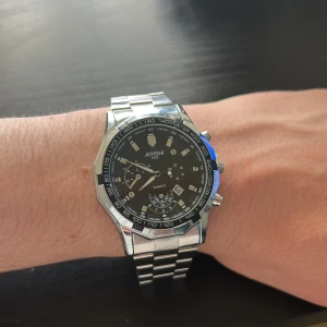 AIYISHI silverfärgad herrklocka - Stilren herrklocka från AIYISHI med svart urtavla och silverfärgat armband i metall. Klockan har flera små urtavlor, tachymeter runt boetten och tydliga indexmarkeringar. Klassisk design som passar dig som gillar sportig och modern look.