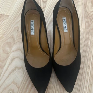 Svarta pumps från footlight - Klassiska svarta pumps från Footlight i mjuk mocka med spetsig tå och smal klack. Snygg och tidlös modell som är tillverkad i Italien. Perfekta för dig som gillar stilrena och eleganta skor.