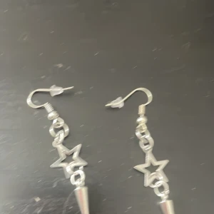 Silvriga örhängen med stjärna och spike - Coola silvriga örhängen med öppen stjärnform och hängande konformad spike. De har krokar med transparenta pluppar och ger en edgy vibe till din stil. Perfekta för dig som gillar unika detaljer och statement-accessoarer.