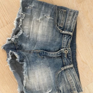 Blå jeansshorts med fransig kant - Snygga blå jeansshorts med slitna detaljer och fransig kant. Klassisk femficksmodell med knapp och dragkedja framtill. Perfekta för sommaren och ger en avslappnad vibe. Passar dig som gillar en lite coolare stil❤️