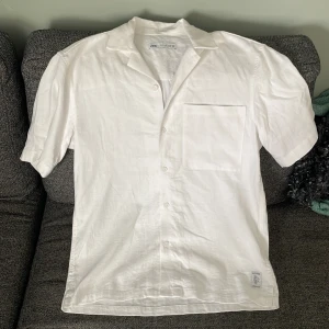 Vit linneskjorta från Zara - Snygg vit skjorta från Zara i luftigt linne. Skjortan har korta ärmar, klassisk krage, knäppning framtill och en bröstficka. Perfekt för varma dagar och enkel att styla till olika outfits.