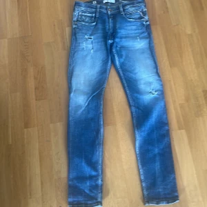 Blå Replay jeans med slitningar - Snygga blå jeans från Replay med slitna detaljer och lätt tvättad look. Klassisk femficksmodell med normal passform och raka ben. Perfekta för dig som gillar en avslappnad och trendig stil. Strl 32/34