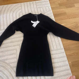 Svart figursydd stickad klänning - En svart, tight stickad klänning från gina med lång ärm och rund hals. Klänningen är kort och har en enkel, stilren design som passar perfekt till sneakers eller boots. Superenkel att styla och känns både trendig och bekväm.