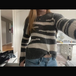 Zebramönstrad stickad tröja  - Mysig stickad tröja från Mango med zebramönster i mörkgrått och beige. Tröjan har en loose passform, rund halsringning och långa ärmar. Perfekt för lager-på-lager och att styla med jeans för en chill look.