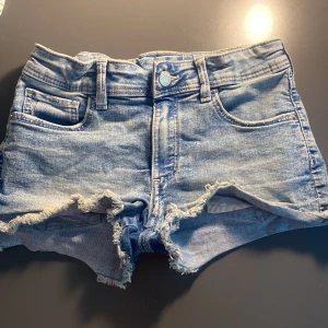 Blå jeansshorts med fjärilsbroderi - Snygga ljusblå jeansshorts med fransig kant och coolt broderat fjärilsmotiv på ena bakfickan.