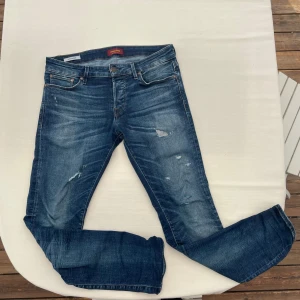 Slim jeans från Jack & Jones - Snygga blå slim fit jeans från Jack & Jones, modell Slim/Glenn. Jeansen har slitna detaljer och klassisk femficksdesign. Tillverkade i jeansmaterial med snygg tvätt och kontrastsömmar. Perfekta för en avslappnad och trendig look.