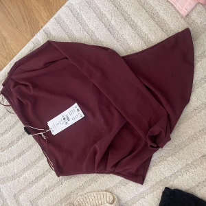 Vinröd topp med asymmetrisk fåll - Säljer en vinröd topp med snygg asymmetrisk fåll. Toppen har en enkel och stilren design som ger en cool vibe. Perfekt för dig som vill sticka ut lite extra med en unik form. Färgtonen är mörk vinröd och materialet känns mjukt och följsamt.