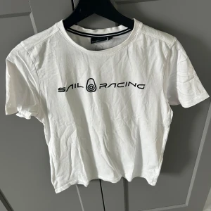 Vit Sail Racing t-shirt  - Vit t-shirt från Sail Racing med svart logotyptryck på bröstet och en mindre logga i nacken. Säljs pågrund av att den inte används och bara står i garderoben. Använd nån gång men är som helt ny. Stryker t-shirtsen innan jag fraktar iväg den. Bara att skriva vid frågor eller fler bilder. Storlek 170.