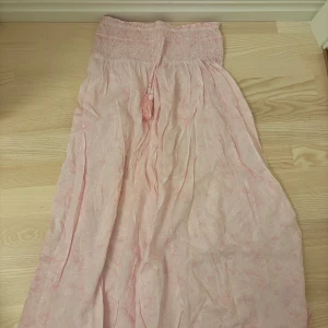 Ljusrosa kjol Gina Tricot - Supersöt ljusrosa kjol från Gina Tricot med paisleymönster, smock upptill och dekorativa tofsar med pärlor. Kjolen har en luftig känsla och är perfekt för varma dagar. Materialet känns lätt och flowy, och färgen är riktigt somrig.