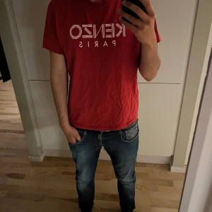 Röd Kenzo t-shirt - Säljer en röd t-shirt från Kenzo med vit grafisk logga 'KENZO PARIS' på bröstet. Klassisk rund halsringning och korta ärmar. Perfekt för en clean och stilren look. Ett hål på t-shirten.