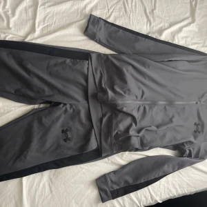 Grå träning tracksuit av Under Armour - Snygg grå tracksuit från Under Armour med svart logga på bröstet. Säljer då dem inte används  längre och har inga skador eller så. Går att köpa separat med