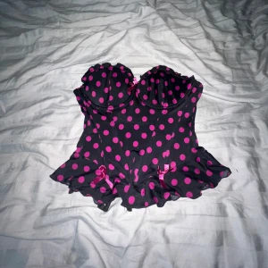 Svart korsett med rosa prickar H&M - Supersöt korsett från H&M i svart med rosa prickigt mönster. Fick som present men inte riktigt min stil. ”Bh-banden” går att ta av om man så vill det 🫶