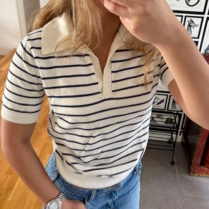 Randig Tröja från & Other Stories - Superfin krämvit pikétröja från & Other Stories med marinblå ränder. Tröjan har klassisk krage, kort ärm och mjukt stickat material. Perfekt till jeans eller kjol för en chill och stilren look.