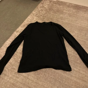 Svart långärmad v-ringad tröja - En stilren svart långärmad tröja från 15Z i storlek M. Tröjan har en klassisk v-ringning och är tillverkad i ett mjukt material som passar perfekt till lager-på-lager. Enkel och clean look som funkar till många outfits.