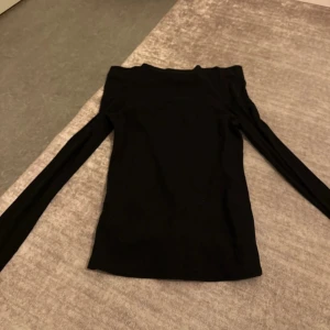 Svart offshoulder långärmad topp - Snygg svart offshoulder topp med långa ärmar. Tight passform och stilren design som passar perfekt till jeans eller kjol. Mjuk och stretchig bomullskänsla som gör den bekväm att bära. Enkel men trendig look för dig som gillar minimalistiskt.